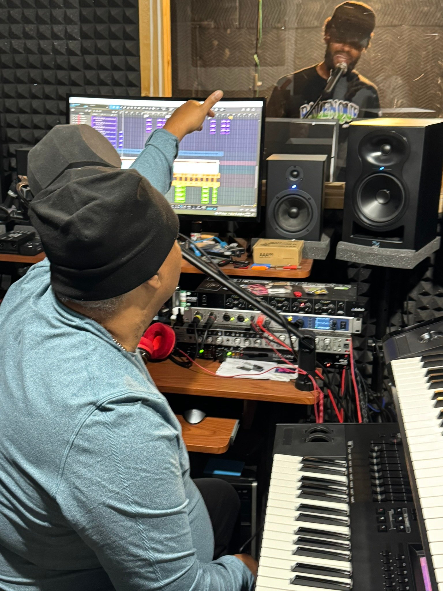 Producer and vocalist collaborating in a recording studio with keyboards and audio equipment